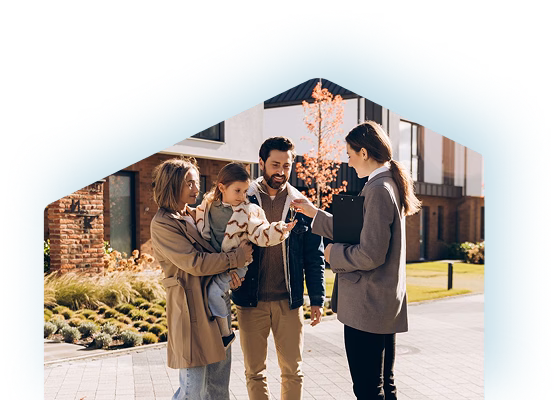 A couple holding their toddler talks with a real estate agent outside a modern home, sharing a welcoming moment in warm autumn light.
