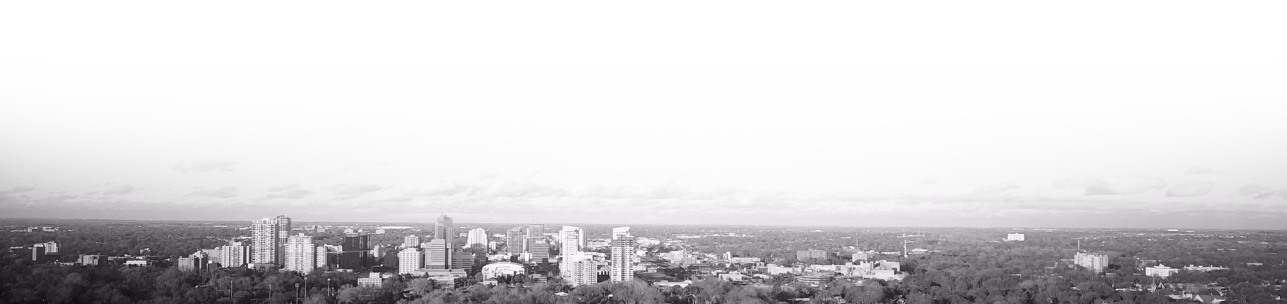 A wide black-and-white panorama of the London skyline, with clusters of mid-rise buildings beneath a dark, overcast sky, creating a subdued mood.